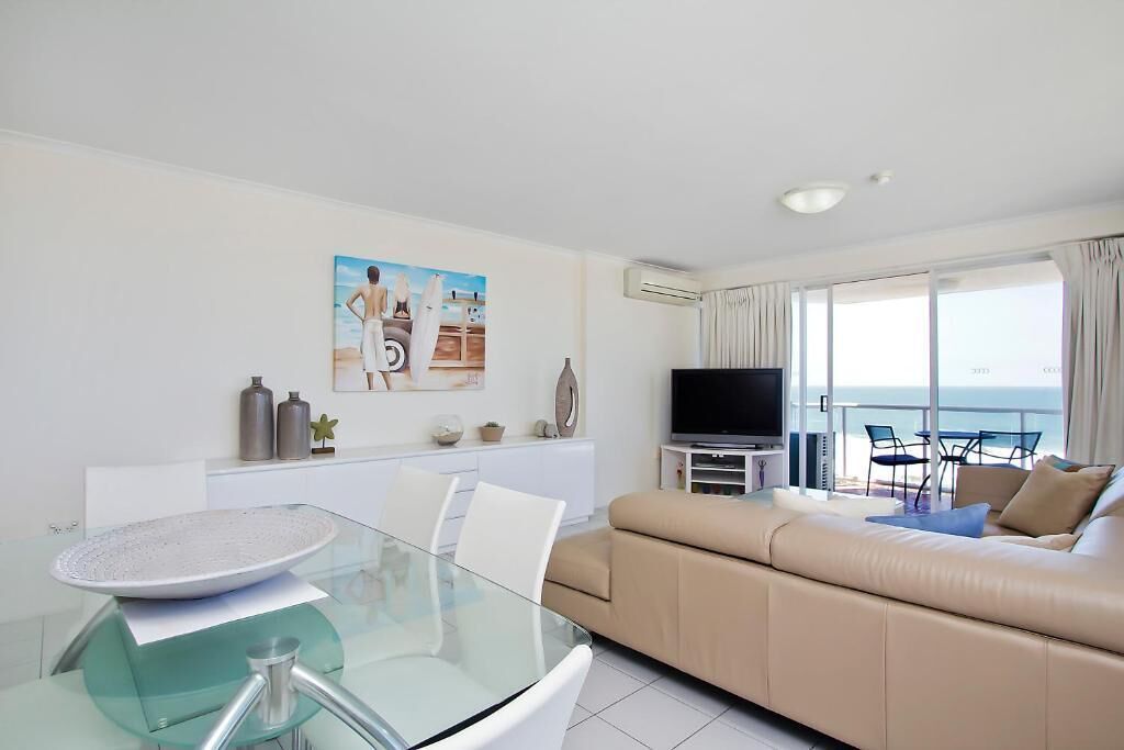 A modern living room with a glass dining table, beige sofa, and a TV.