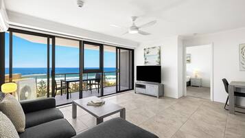 A modern living room with a large sliding glass door leading to a balcony with a view of the ocean.