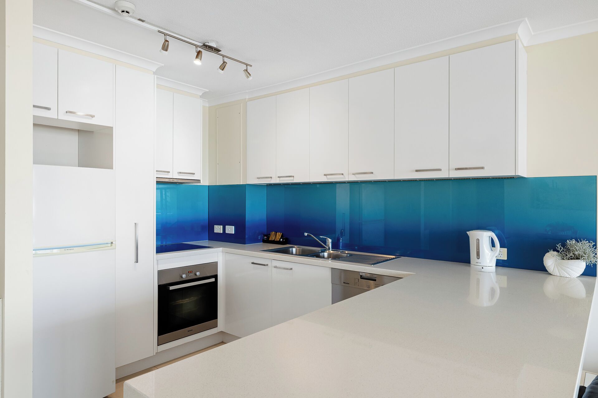 A modern kitchen with white cabinetry, a blue backsplash, and stainless steel appliances.