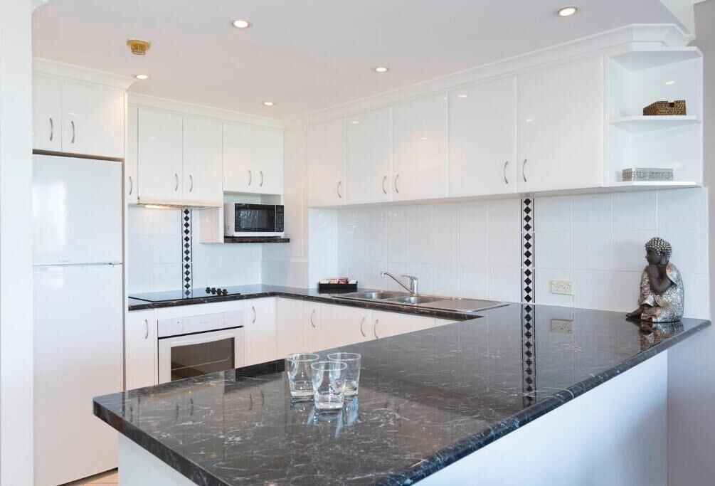 A modern kitchen with white cabinets, a black countertop, and a microwave.