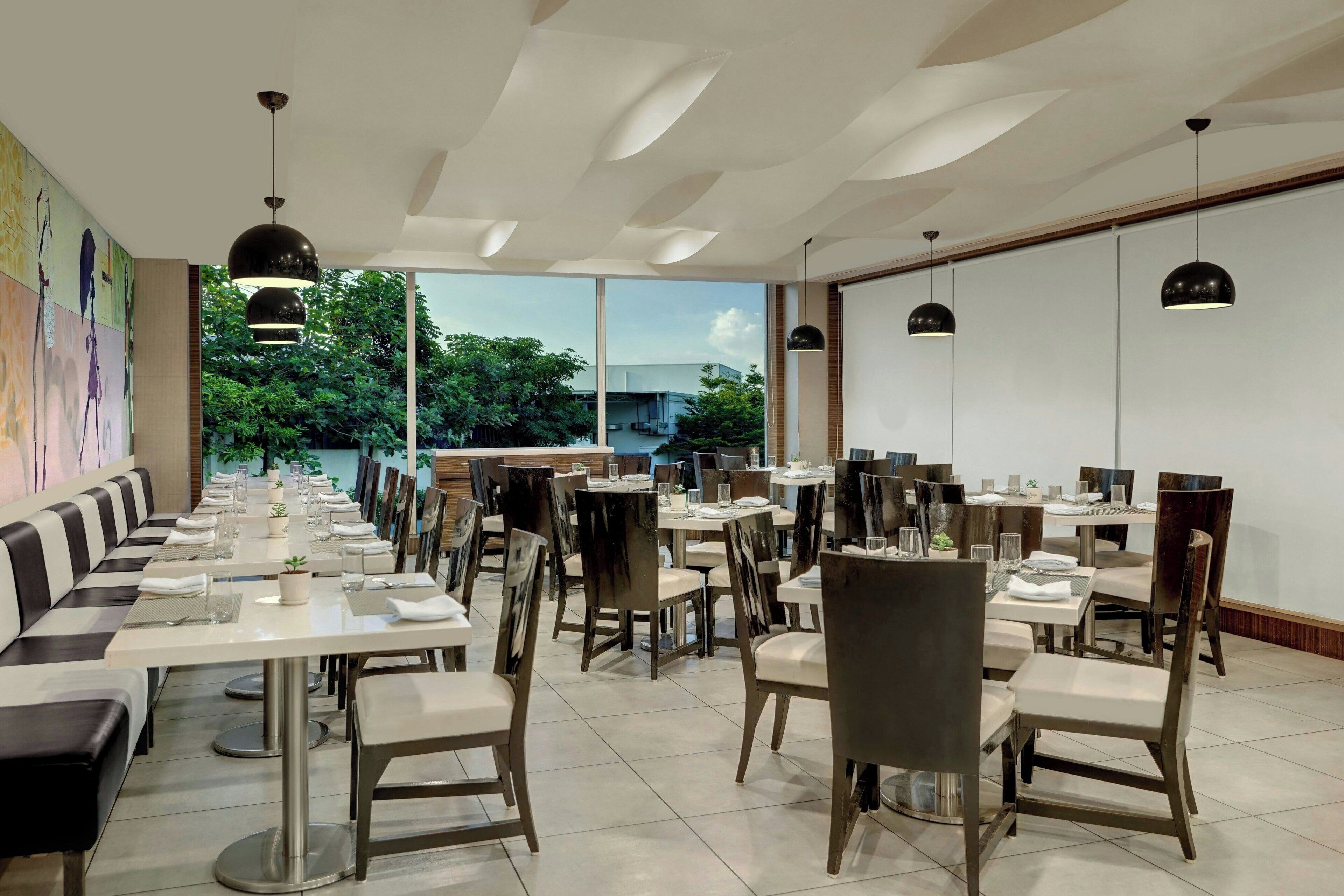 Un restaurante moderno con una larga mesa compartida, mesas individuales e iluminación colgante negra.