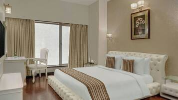 A hotel room with a large bed, a desk, a chair, and a window with curtains.