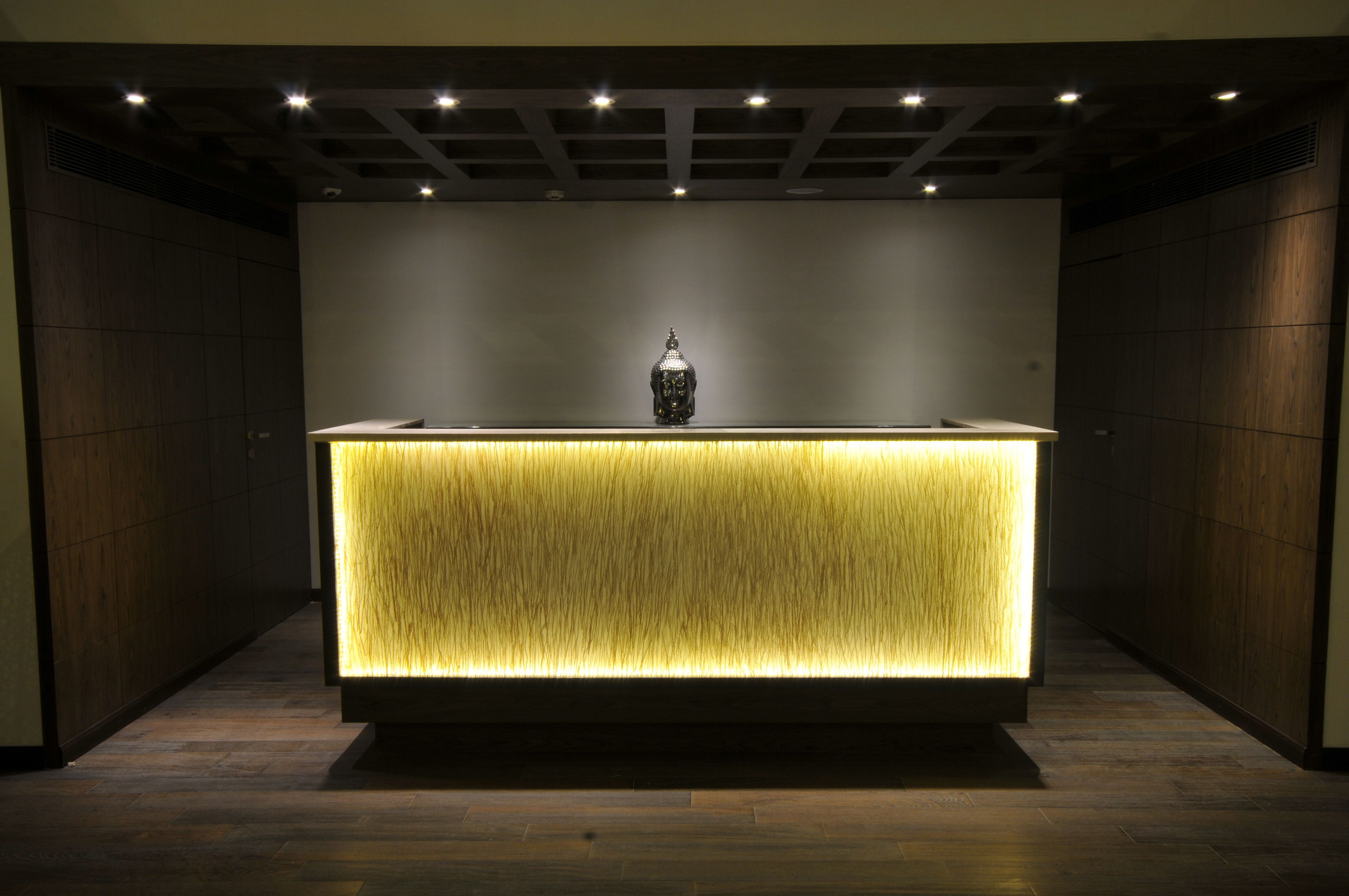 Uma receção com um painel iluminado com textura e um objeto decorativo em cima.