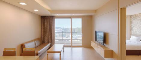 A modern hotel room with a sofa, a small table, a TV, and a bed.
