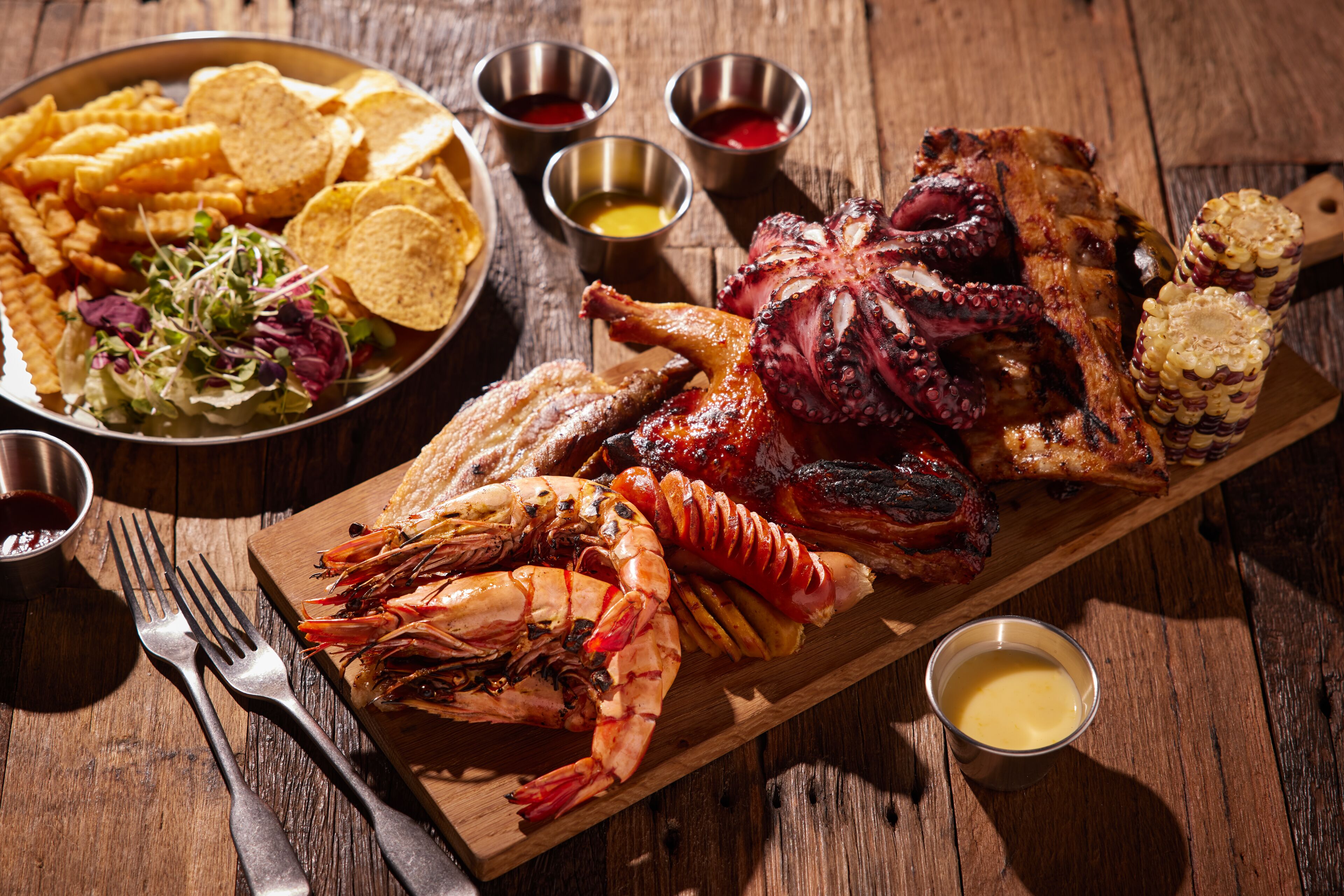 A wooden table with a variety of seafood including grilled octopus, shrimp, and corn on the cob.