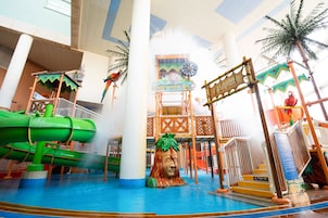 An indoor water park with a water gun play zone, a central fountain, and a tropical-themed play structure.