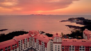 A coastal hotel with multiple buildings featuring red roofs and balconies, overlooking a beach and the sea. - Sono Belle Byeonsan (Buan)