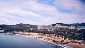 A large hotel with multiple buildings, situated on a coastal area with a beach and mountains in the background. - Sono Belle Byeonsan (Buan)