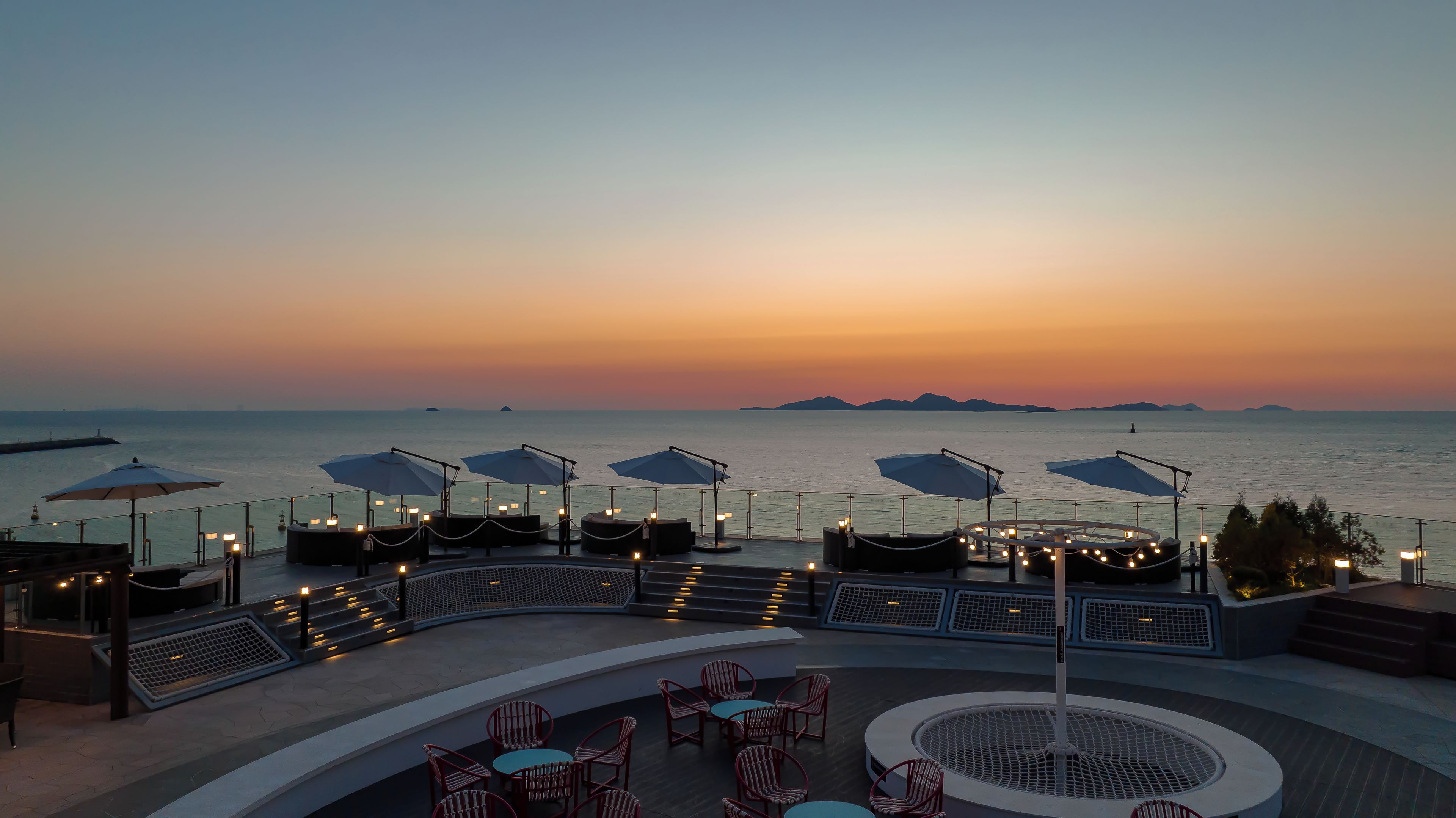 A waterfront terrace with outdoor seating and umbrellas, overlooking the sea.