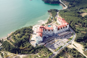 An aerial view of a hotel with a red-roofed building, a parking lot, and a beach area.
