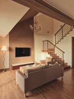 A modern living room with a large flat-screen TV, a sofa, a coffee table, and a staircase.