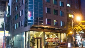 A modern hotel with a glass facade, multiple floors, and a well-lit entrance. - Green World JianPei (Taipei)