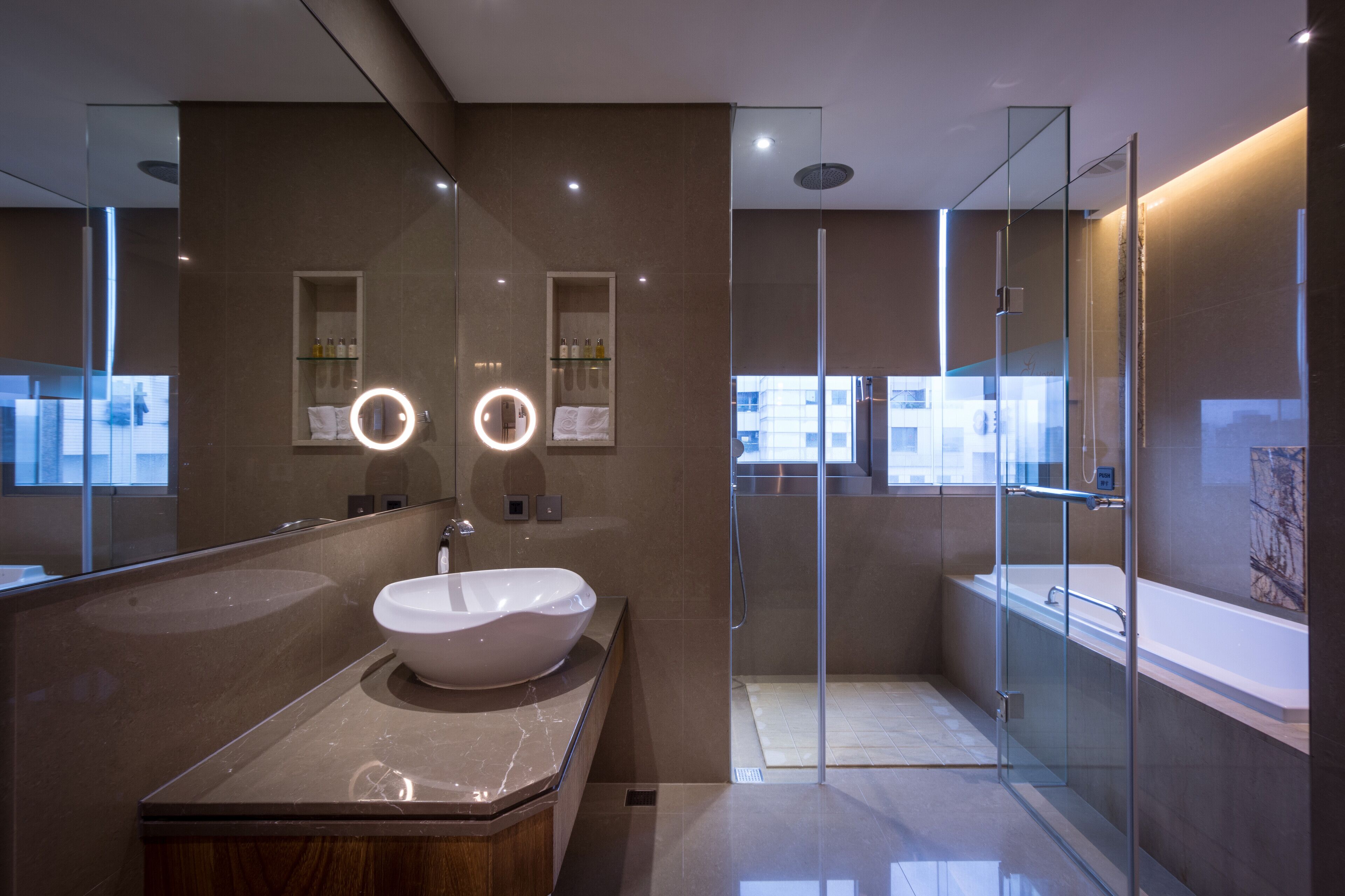 Un baño moderno con un espejo grande, un lavabo sobre encimera, ducha con mampara de vidrio y una bañera.