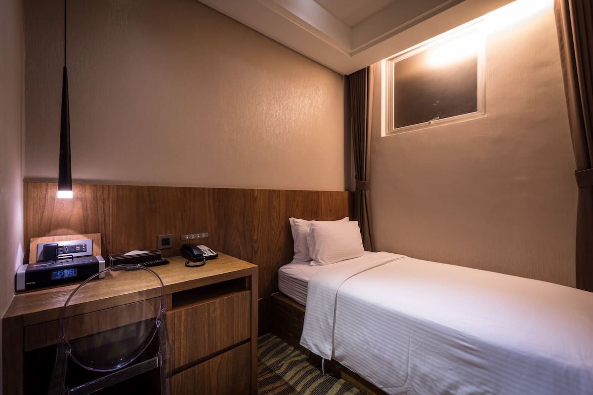 Una habitación de hotel con una cama individual, un escritorio con computadora, un teléfono y una lámpara.