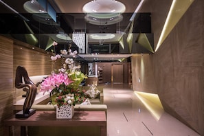 Un hall d’entrée moderne avec un comptoir d’accueil, une sculpture et une composition florale.