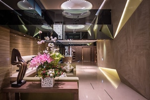 Een moderne lobby met een receptiebalie, een sculptuur en een bloemstuk.