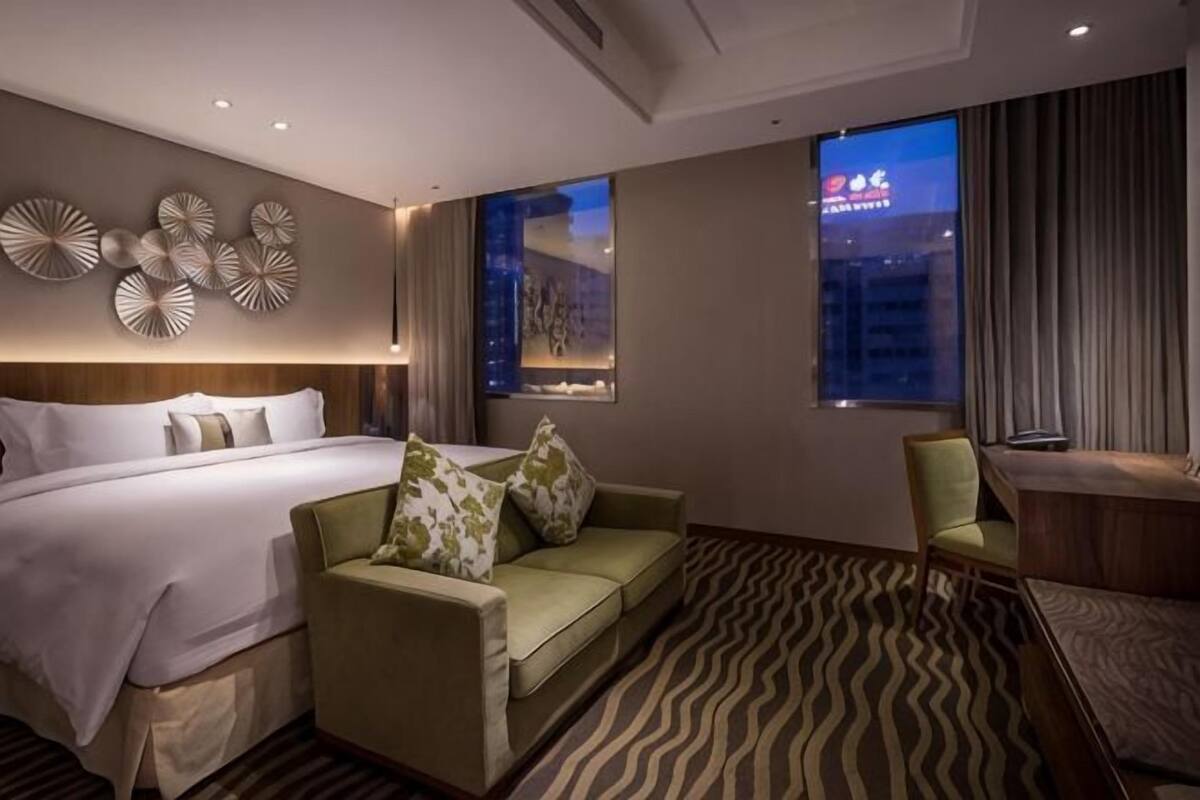 Habitación de hotel con una cama, un sofá verde, un escritorio y vistas a la ciudad.