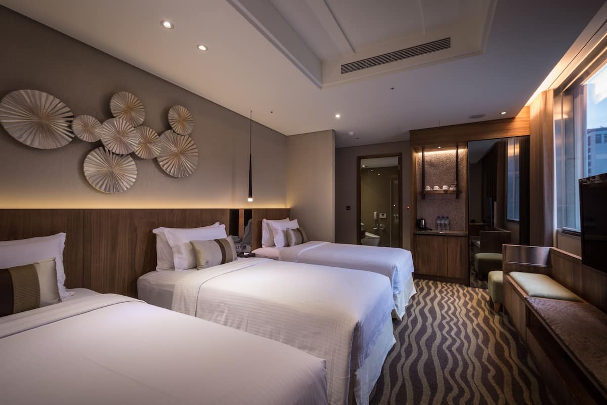 Habitación de hotel con tres camas, zona de estar, minibar y un espejo grande.
