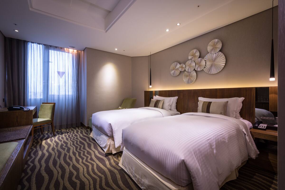 Habitación de hotel con dos camas, un escritorio, una silla, alfombra estampada y un muro decorado con platos.