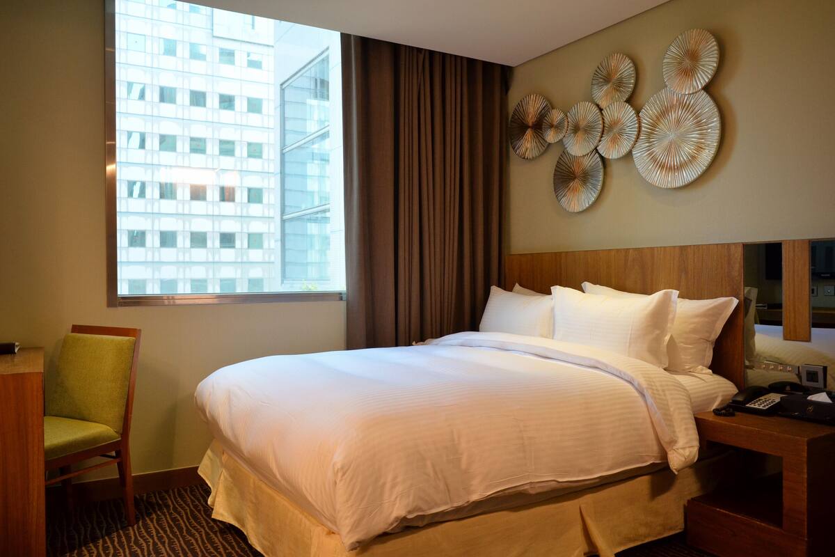 Habitación de hotel con una cama grande, un escritorio, una silla, un ventanal con vistas a un edificio y decoración en la pared.