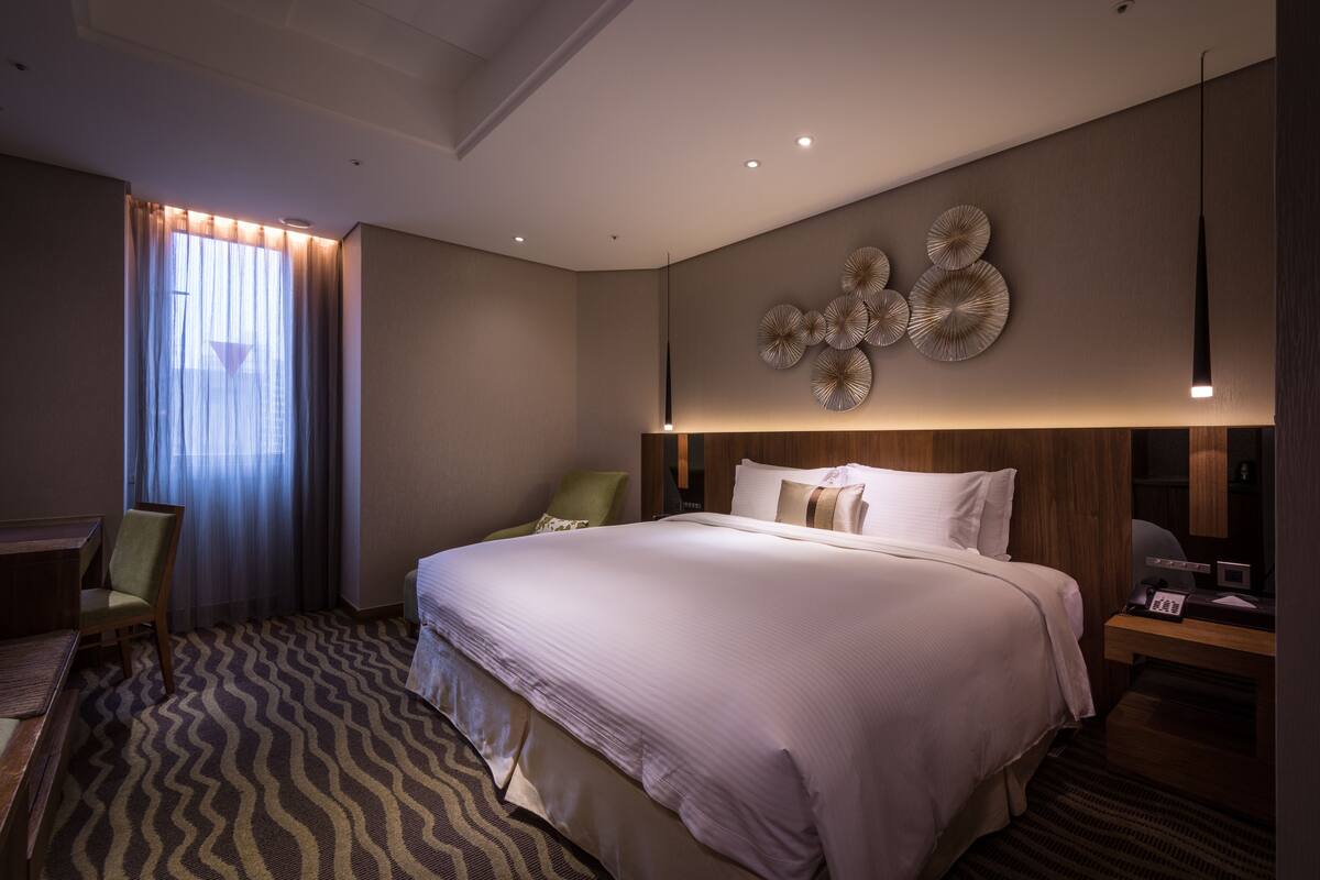 Una habitación de hotel con una cama grande, un escritorio, una silla y una lámpara de pared.