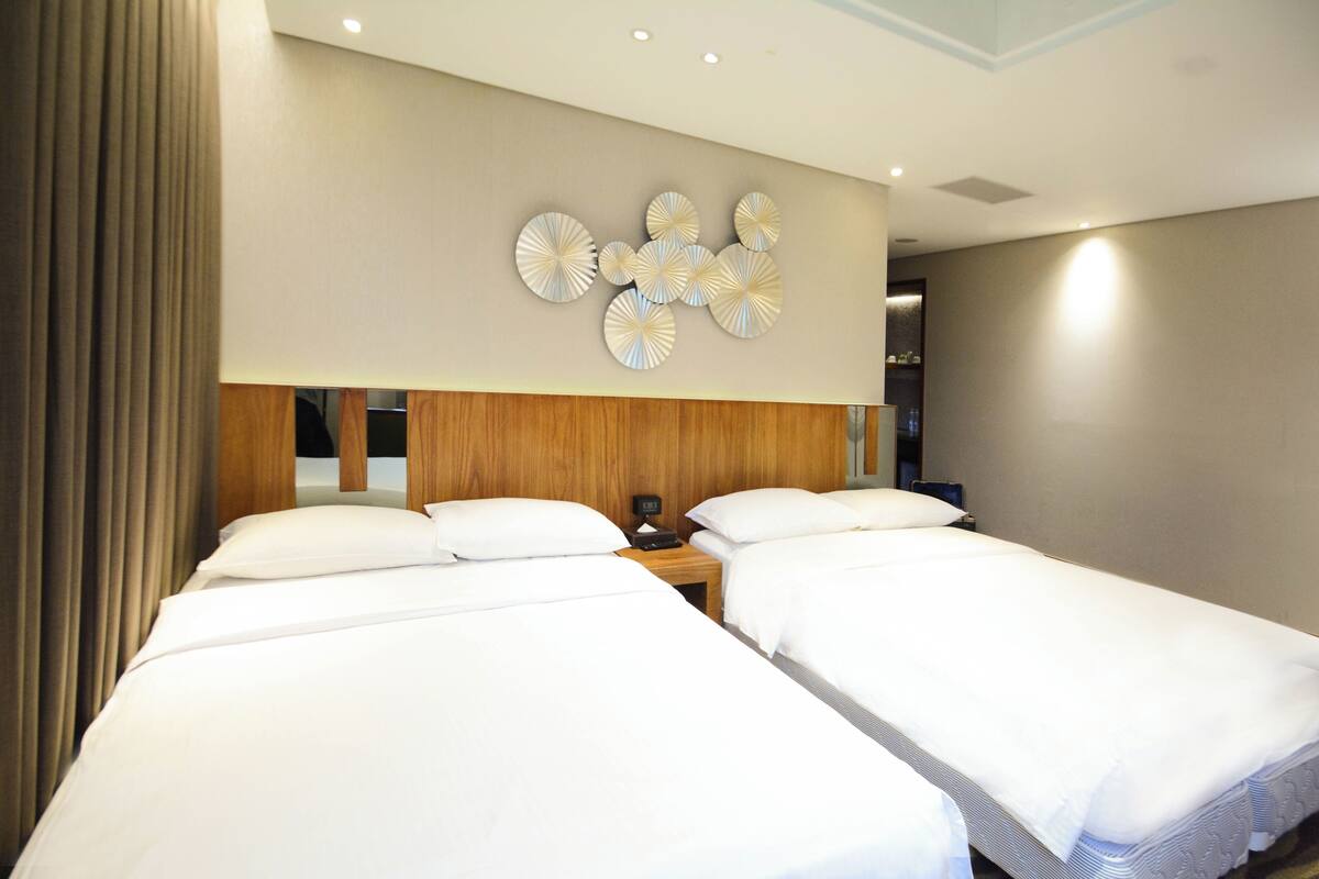 Habitación de hotel con dos camas individuales, cabecera de madera, reloj en la pared y un adorno decorativo.