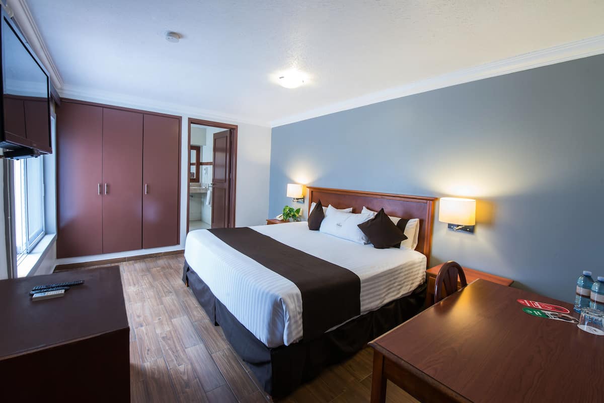 A hotel room with a bed, bedside tables, a desk, a wardrobe, and a window.