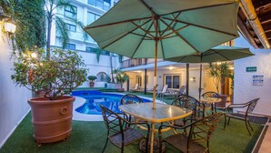 An outdoor patio with a pool, green artificial grass, and a table with chairs and an umbrella. - Del Marqués Hotel and Suites (Guadalajara)