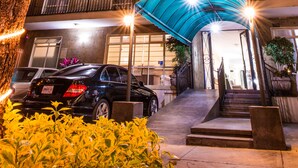 A multi-story building with a covered entrance, outdoor lighting, and a parked car. - Del Marqués Hotel and Suites (Guadalajara)