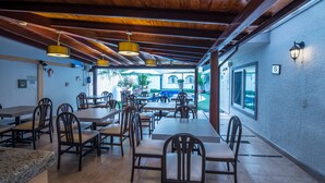 An indoor dining area with wooden tables and chairs, a ceiling with exposed beams, and a view of the outdoor patio. - Del Marqués Hotel and Suites (Guadalajara)