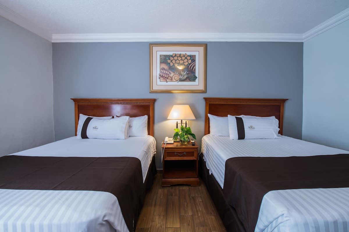 A hotel room with two beds, a nightstand with a lamp, and a framed picture on the wall.
