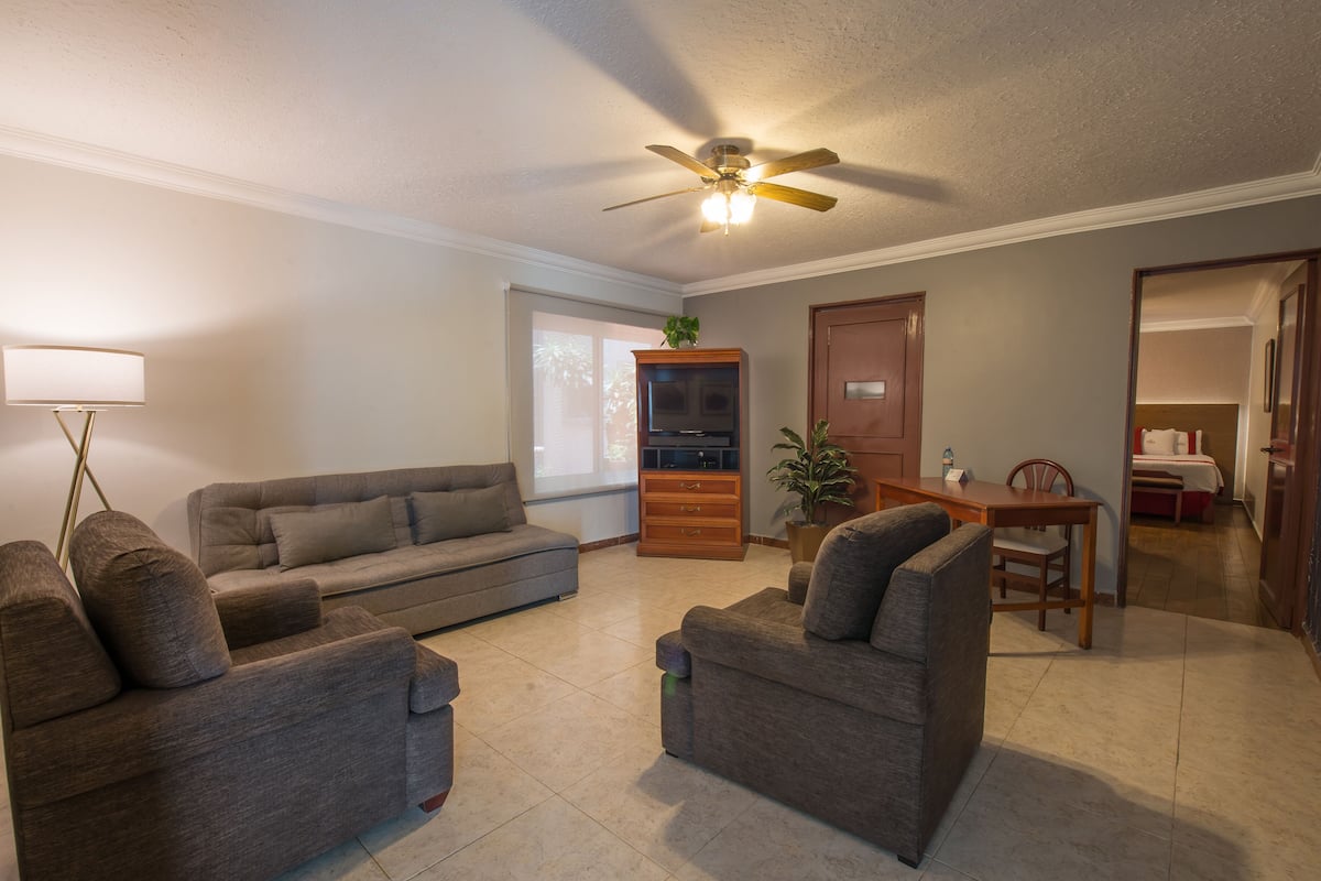 A living room with a sofa, armchairs, a coffee table, a TV stand, and a ceiling fan.
