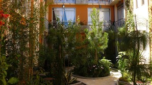 A courtyard with a building featuring balconies, surrounded by various plants and a pathway. - Axkan Arte Hotel San Cristobal (San Cristóbal de las Casas)