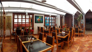 A restaurant with wooden tables and chairs, a tiled floor, and artwork on the walls. - Axkan Arte Hotel San Cristobal (San Cristóbal de las Casas)