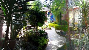 A narrow pathway flanked by lush greenery and potted plants, leading to a building with a mural. - Axkan Arte Hotel San Cristobal (San Cristóbal de las Casas)
