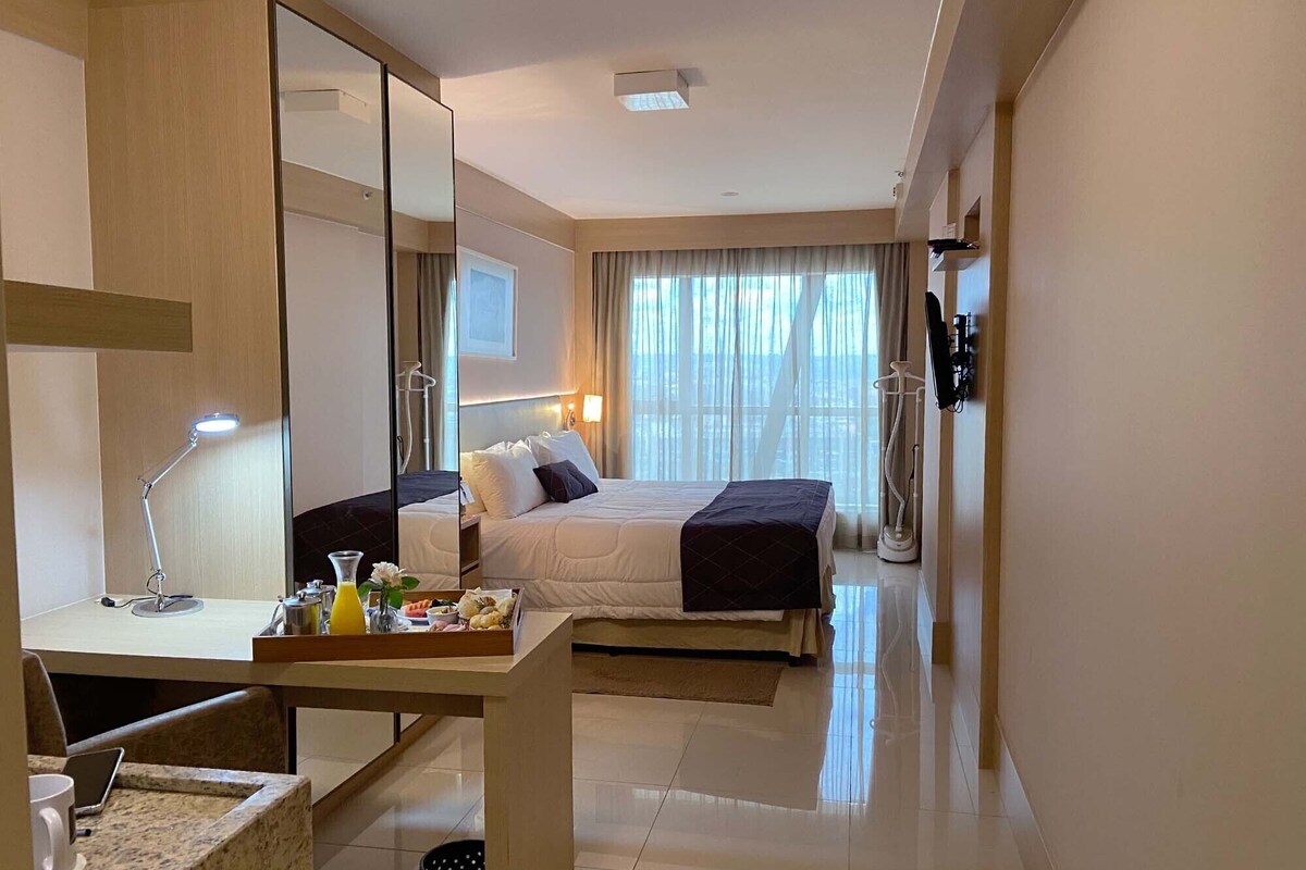 A hotel room with a bed, desk, chair, and a large mirror.