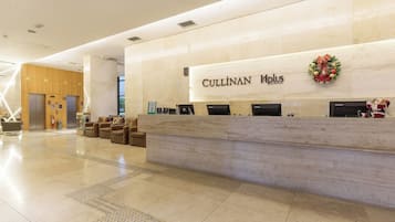 A hotel reception area with a marble counter, a Christmas wreath, and a sign reading "CULLINAN Plus."