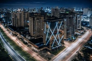 A hotel with a distinctive geometric facade, surrounded by a busy urban street at night. - Cullinan Hplus Premium (Brasília)