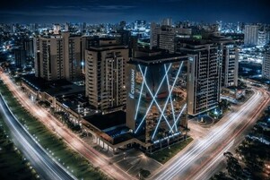 Un hotel con una fachada geométrica llamativa, rodeado de una concurrida calle urbana en la noche.