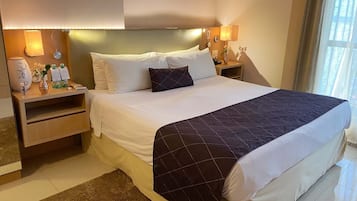 A hotel room with a large bed, two bedside tables, a nightstand, a vase with flowers, a lamp, and a window with curtains.