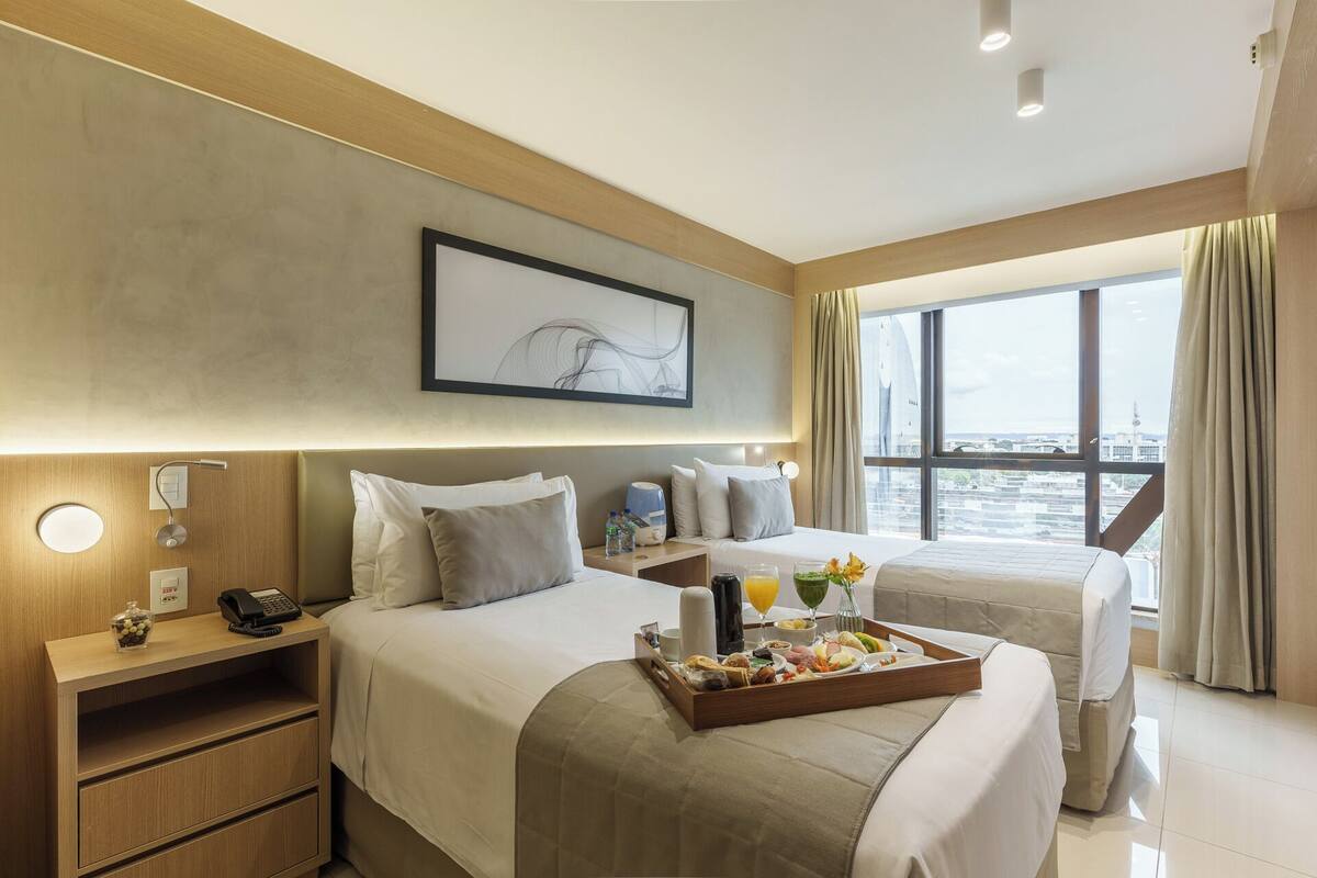 Habitación de hotel con dos camas, un carril para el desayuno, un teléfono y una ventana con vistas.