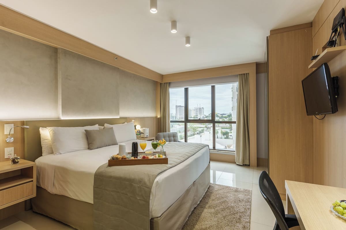 Una habitación de hotel moderna con una cama grande, una mesita de noche y un televisor fijado a la pared.