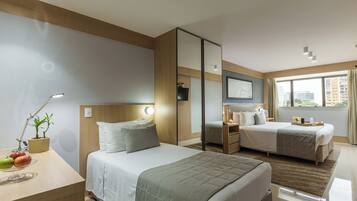 Quarto de hotel com duas camas, uma escrivaninha com abajur, um espelho e uma janela com vista para edifícios.