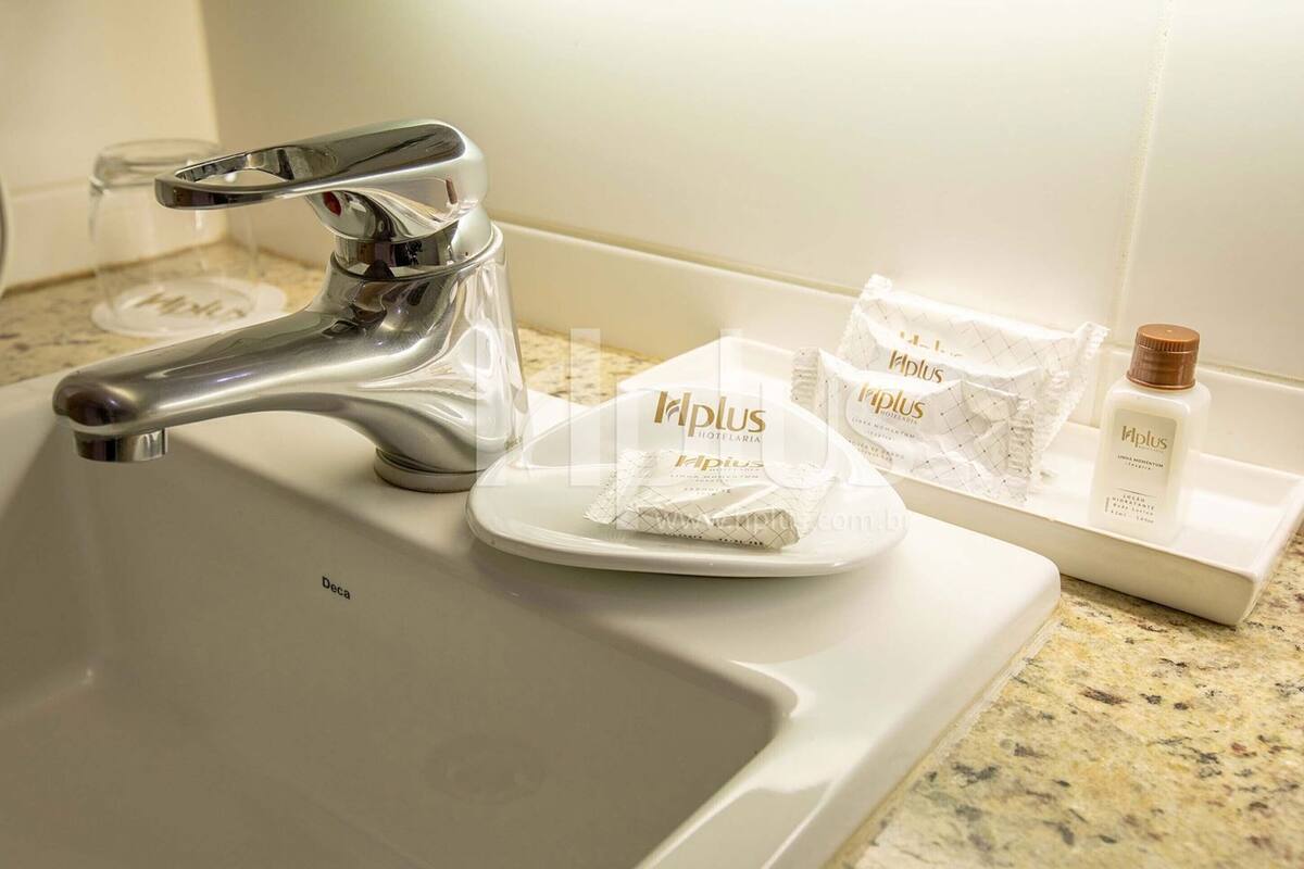 Un lavamanos de baño con un grifo moderno, un dispensador de jabón de vidrio y artículos de aseo, incluyendo una botella y una toalla sobre una bandeja.