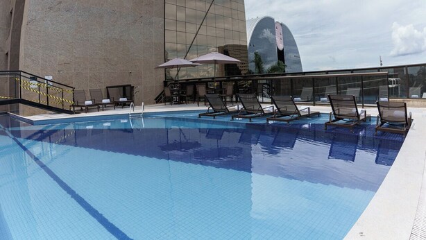 Um hotel moderno com fachada curva singular, área de piscina com espreguiçadeiras e céu claro.