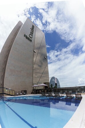 Un hotel moderno con una fachada curva distintiva, un área de piscina con sillones de descanso y un cielo despejado.