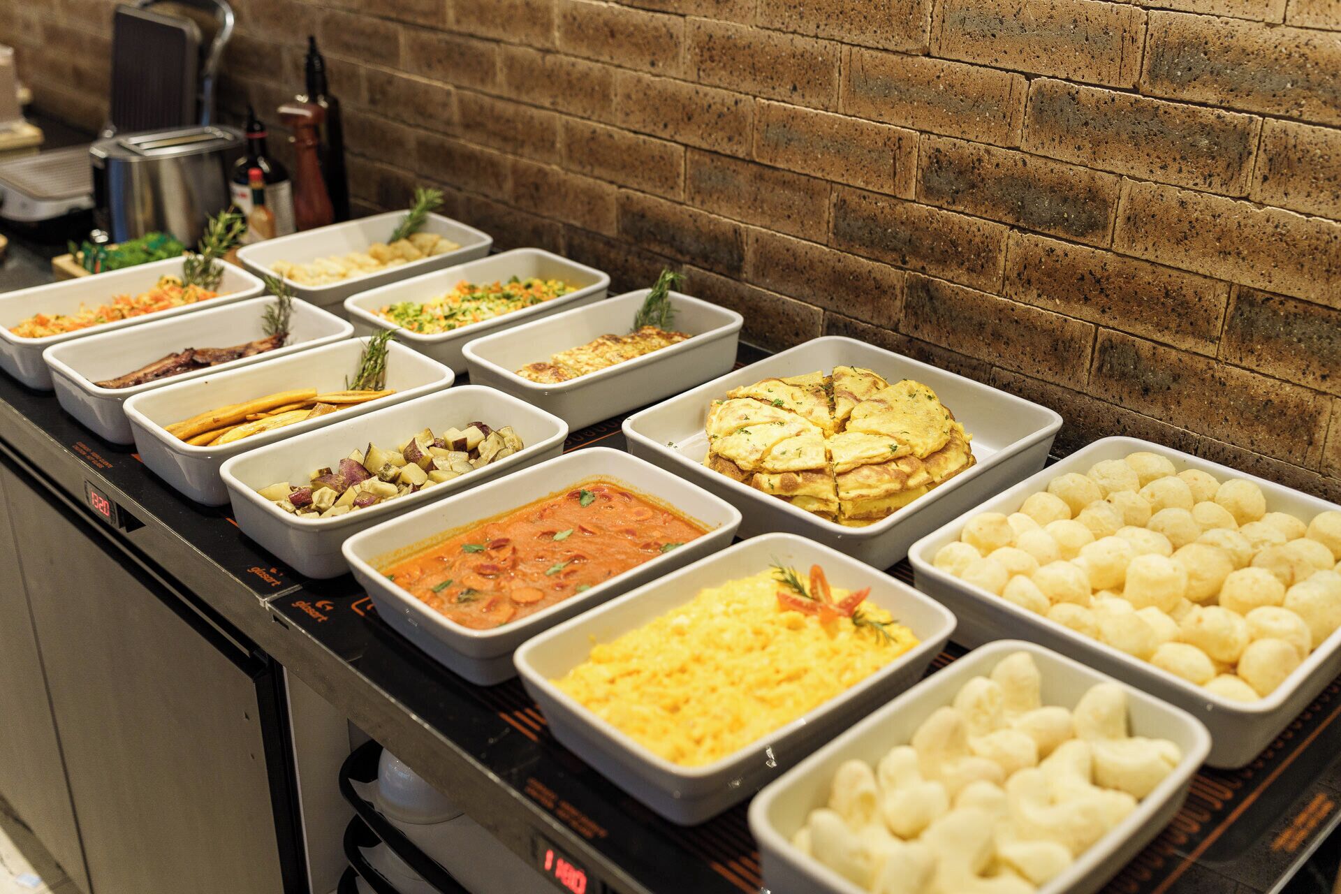 Ein Buffet mit verschiedenen Gerichten, darunter Kartoffeln, eine Tomaten-Speise, Rührei und Käse.