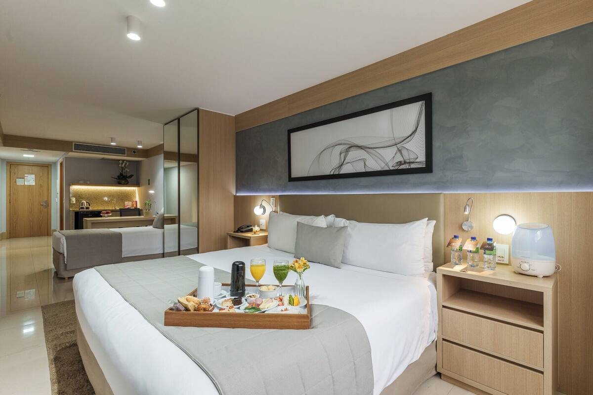 Una habitación de hotel con cama, mesita de noche y una bandeja con alimentos para el desayuno.