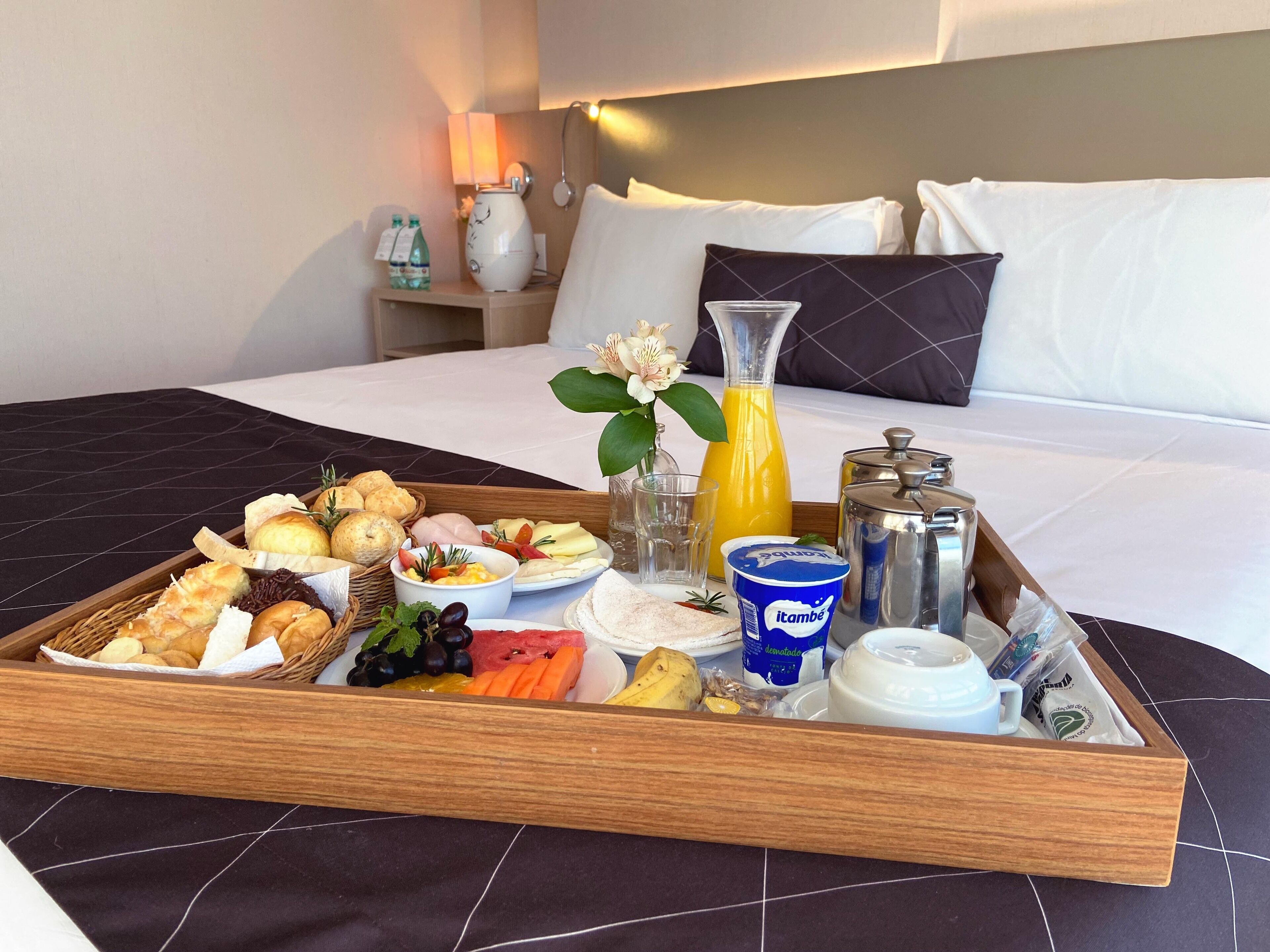 Un vassoio della colazione con pasticcini, frutta e bevande su un letto in una camera d'albergo.