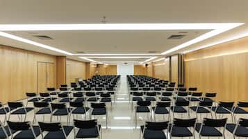 Une salle de conférence avec des rangées de chaises, un pupitre et un écran de projection.